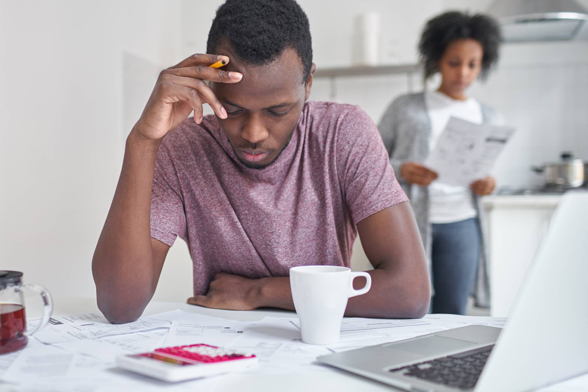 A man looking stressfully down at bills scattered across a table related to housing costs.