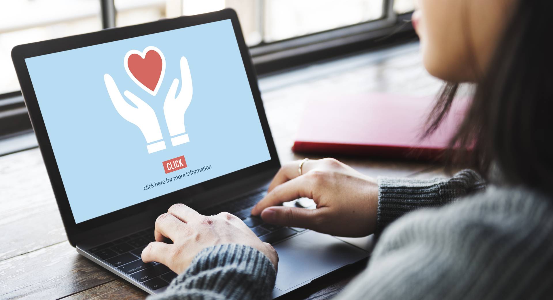 A woman on her laptop looking at an image related to charity with the text "click here for more information."