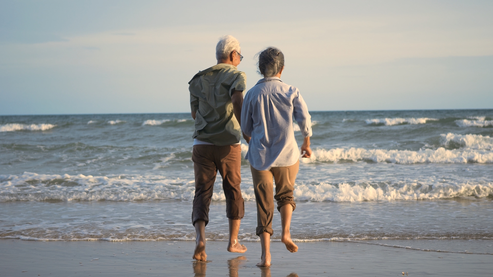 An elderly couple walking towards the beach, enjoying their retirement.