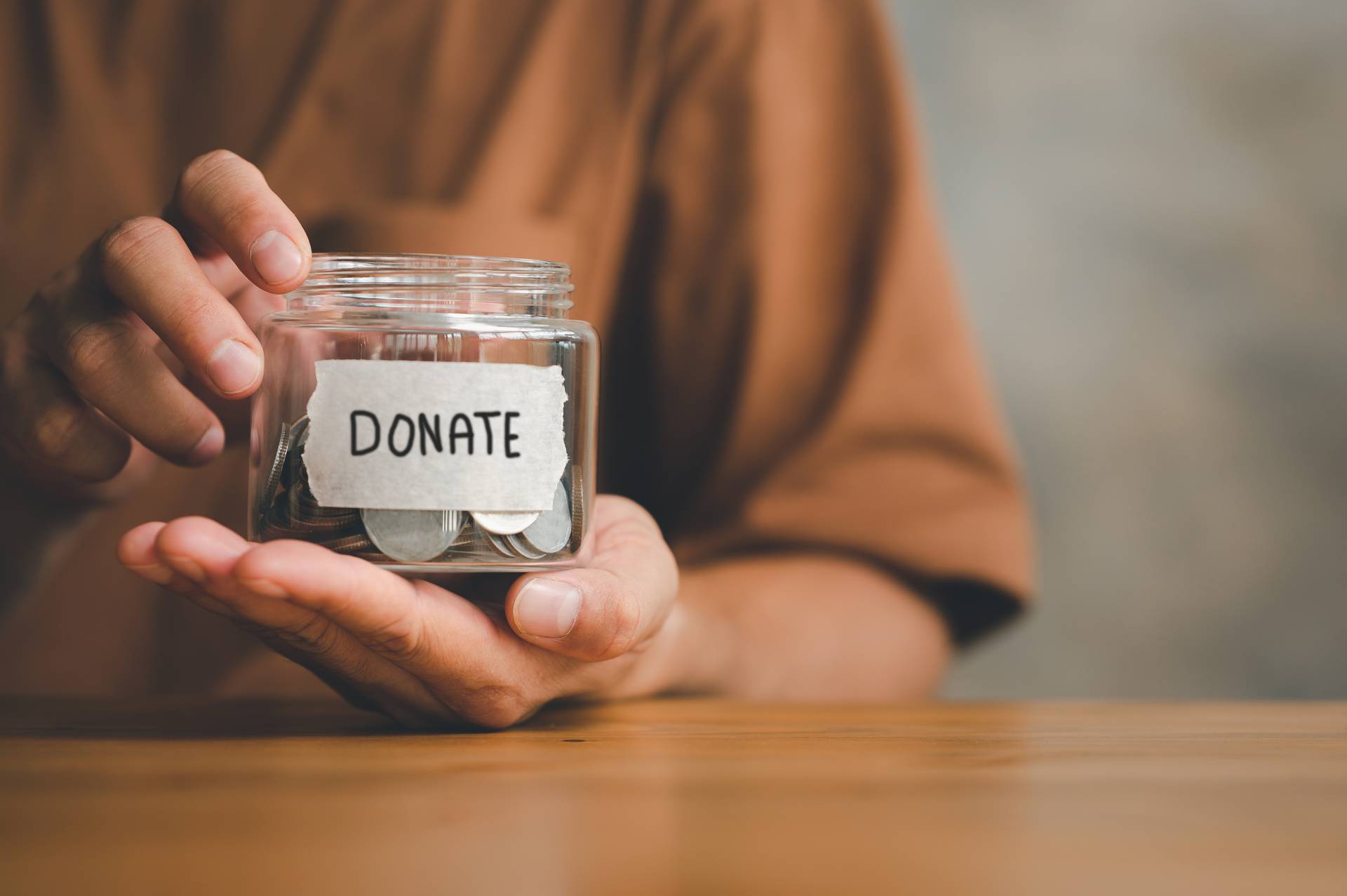 A person holding a glass donation jar that has change in it.