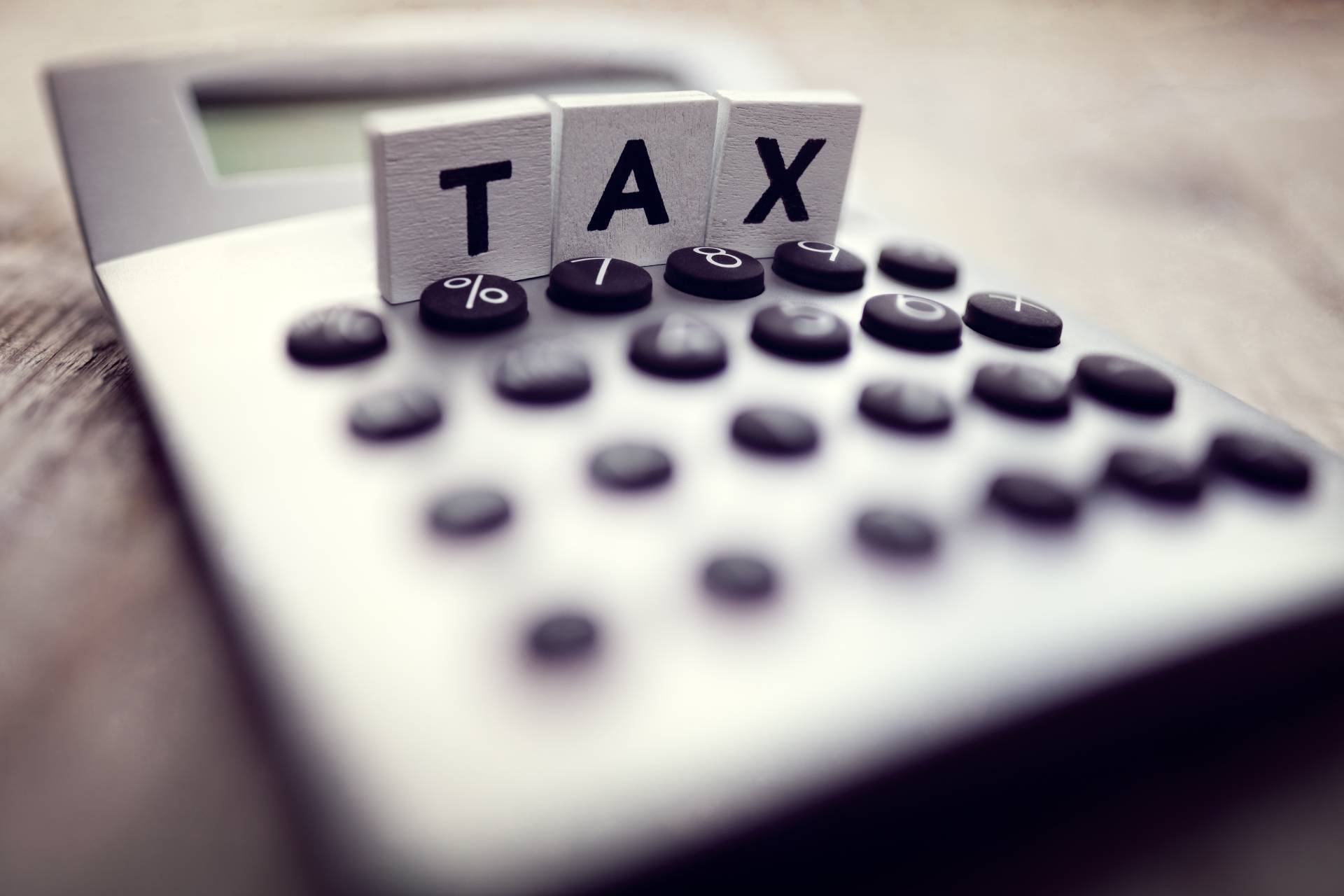 A calculator with three small wooden square blocks on top of it spelling out "tax."