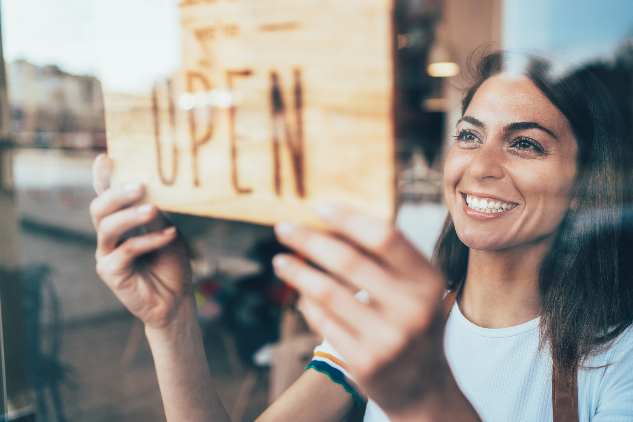 A business owner looking happily as she turns over a sign showing that they are now open.