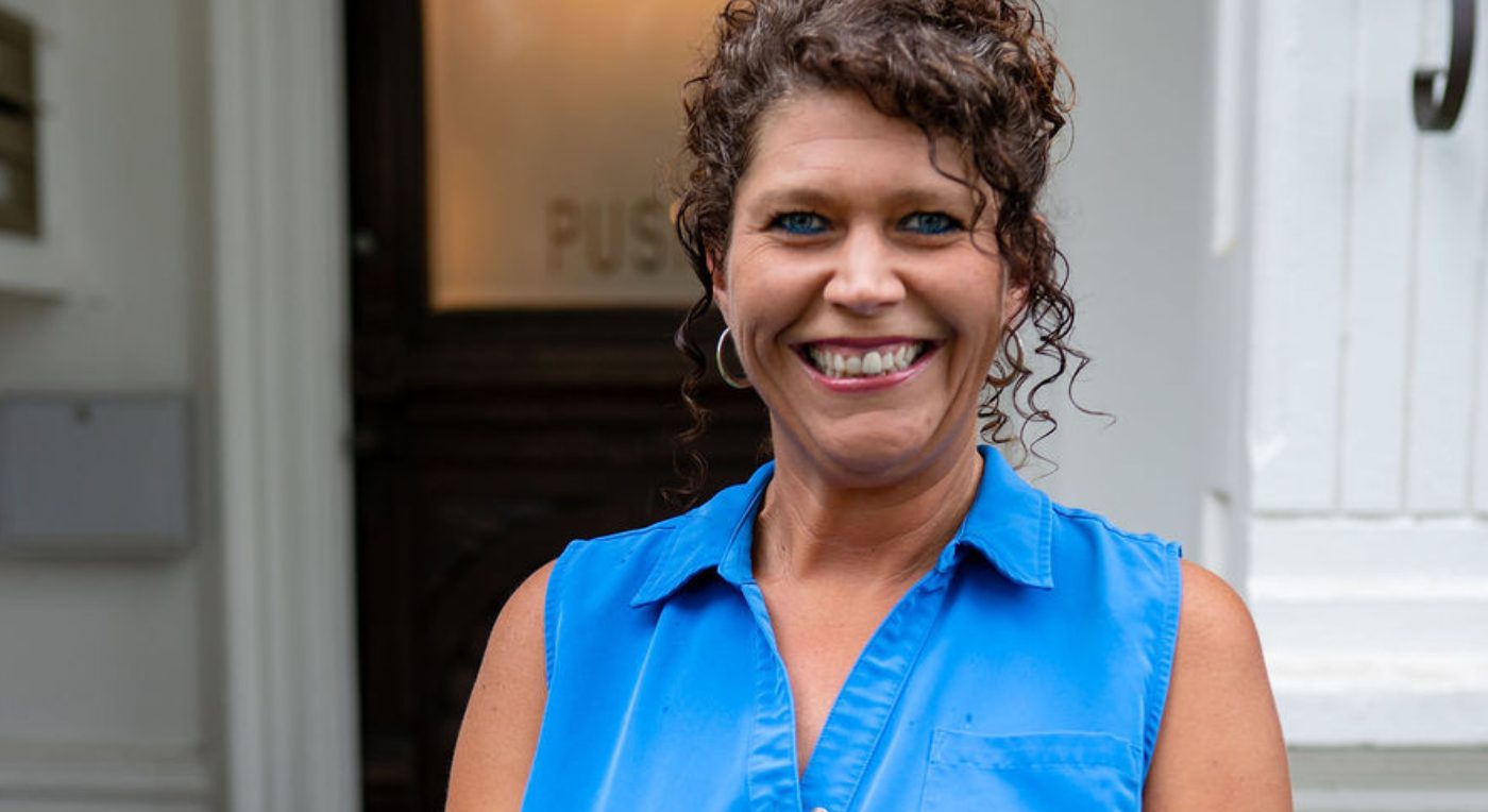 A professional headshot of Ashlee Baggett, a woman with curly brown hair and blue eyes, wearing a bright blue shirt.